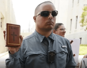 Street preacher Gabriel Olivier, in sunglasses, holding a bible and wearing a body camera.